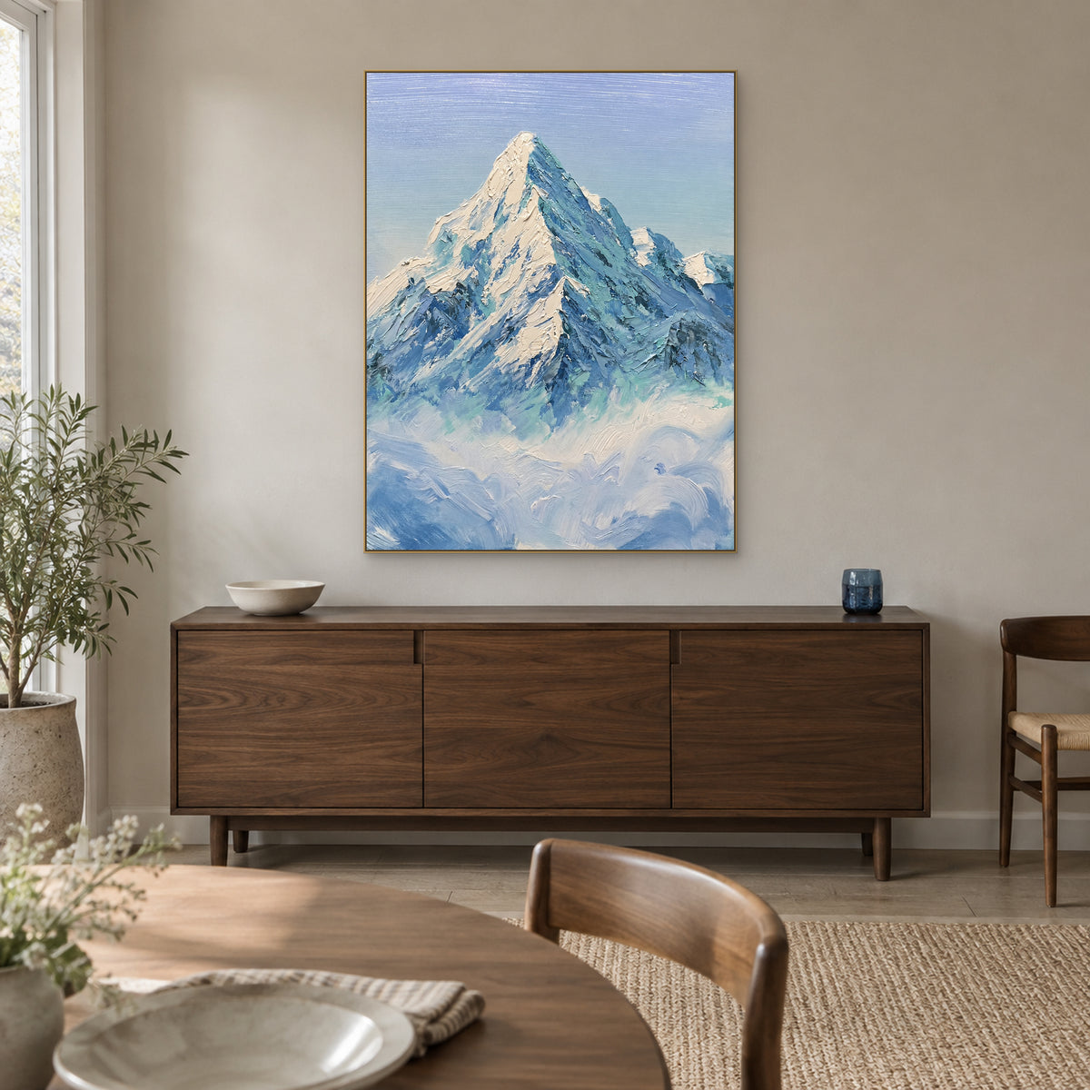Mountain above clouds painting in a champagne-coloured frame, above a dark sideboard in a dining room.