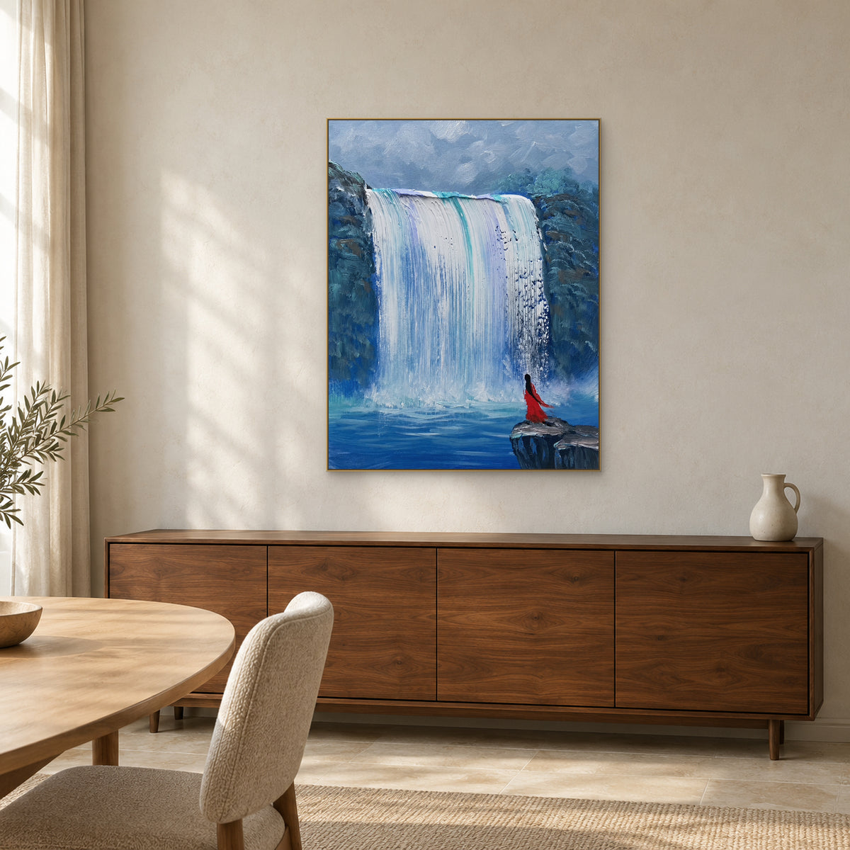 Blue waterfall art in a champagne frame above a walnut sideboard, with an ivory jug and a pale wood dining table nearby.