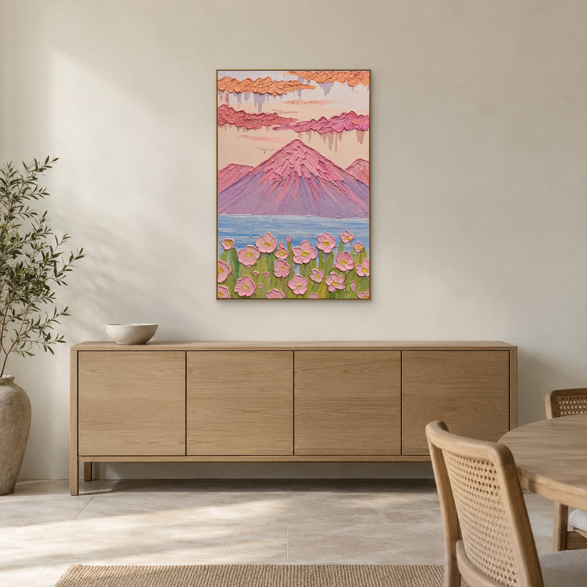 Pink mountain and blue lake painting in a champagne-tone frame above a light wooden dining-room sideboard