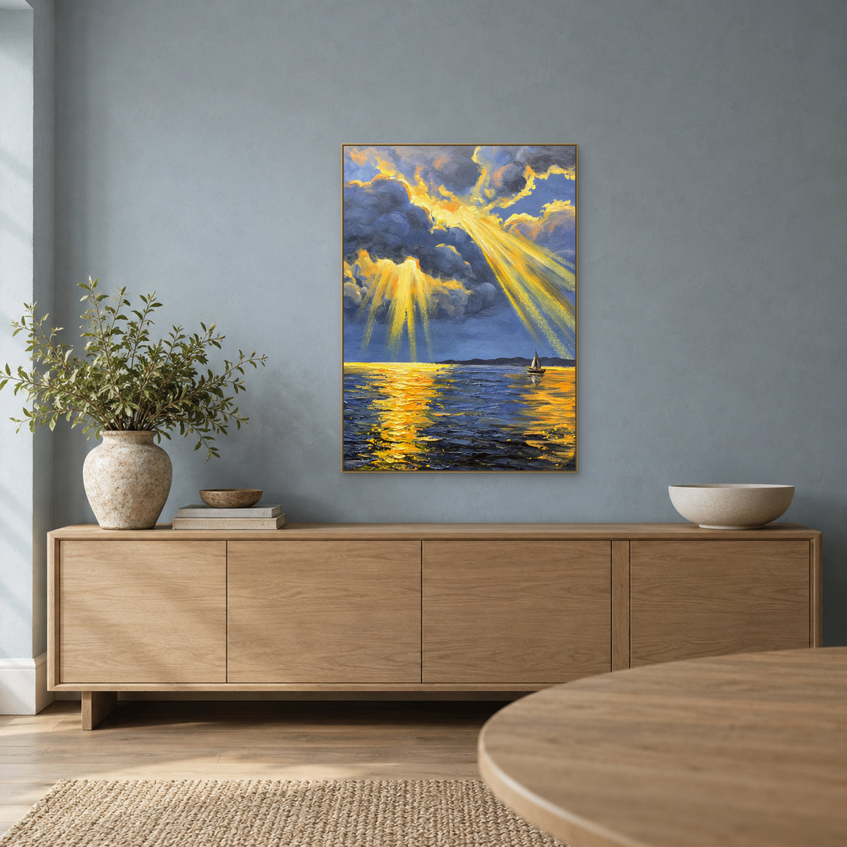 Blue-grey seascape with gold reflections in a champagne-tone frame over an oak sideboard against a blue wall.