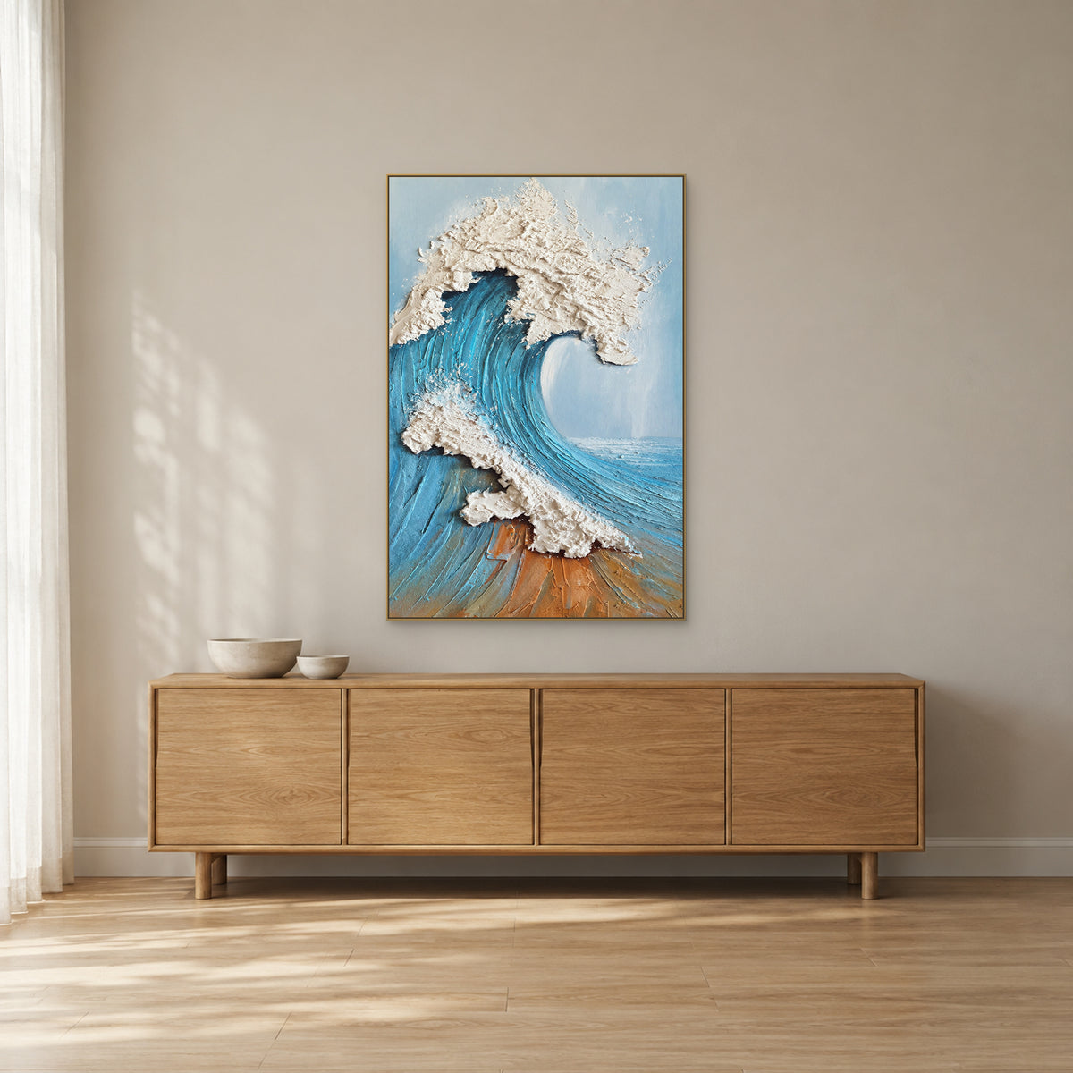 Blue and white wave art in a champagne-tone floating frame above a pale wooden sideboard