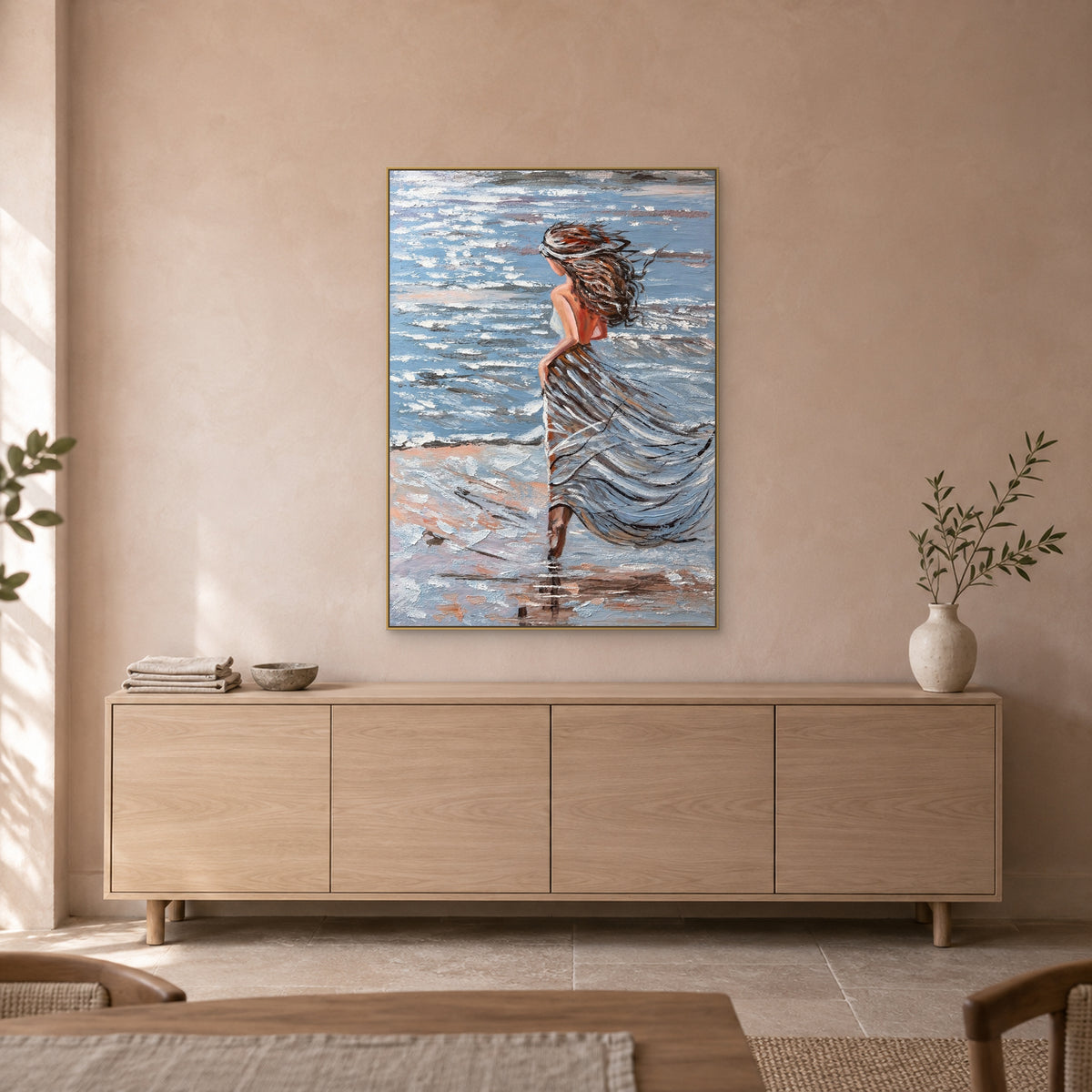 Woman beside the sea in a champagne-toned floating frame above a pale oak-toned sideboard against a blush-beige wall