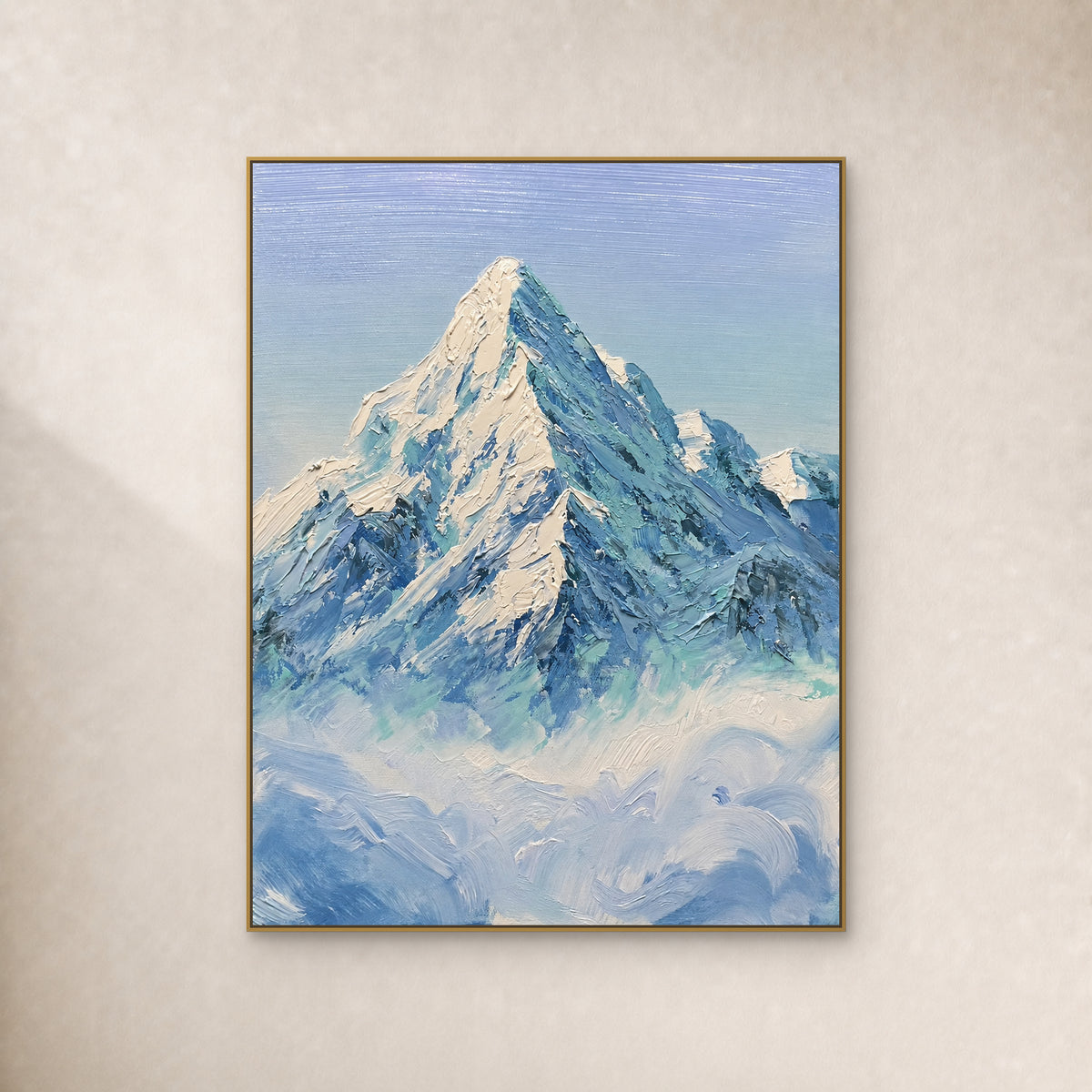 Ivory snow peak and blue-green ridges above clouds, in a slim gold frame on a warm ivory wall.