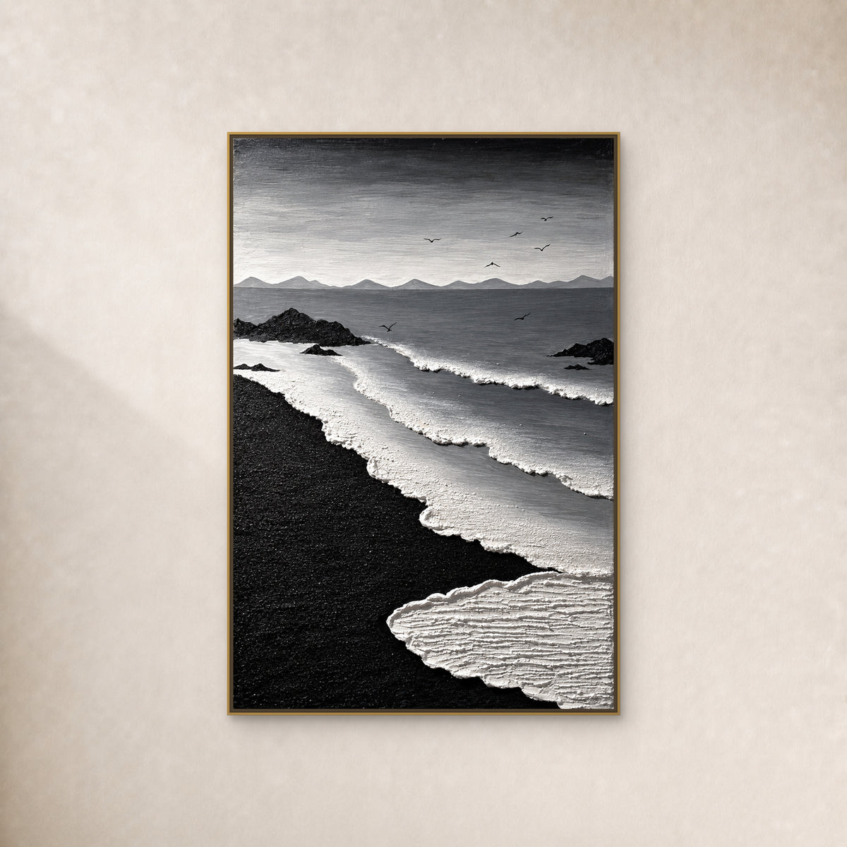Black and white coastal painting with curving surf, black sand and seven birds, in a thin gold-tone floating frame on a warm ivory wall