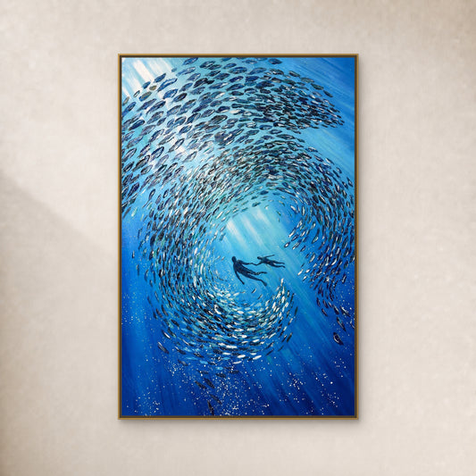 Blue fish spiral around two divers in a thin gold-toned floating frame on a continuous ivory wall
