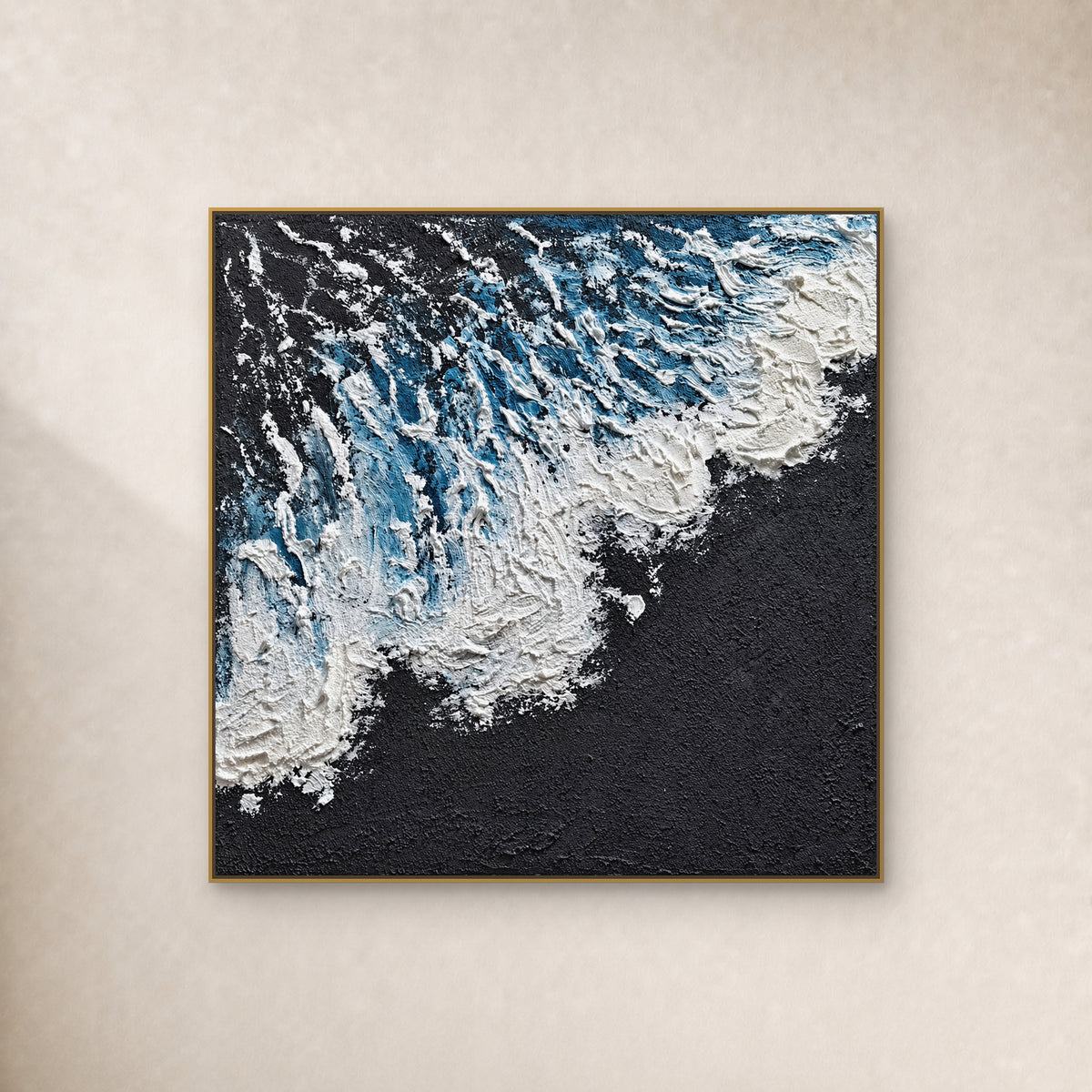 Square blue and white surf painting with a charcoal lower-right field, in a thin gold frame on an ivory wall