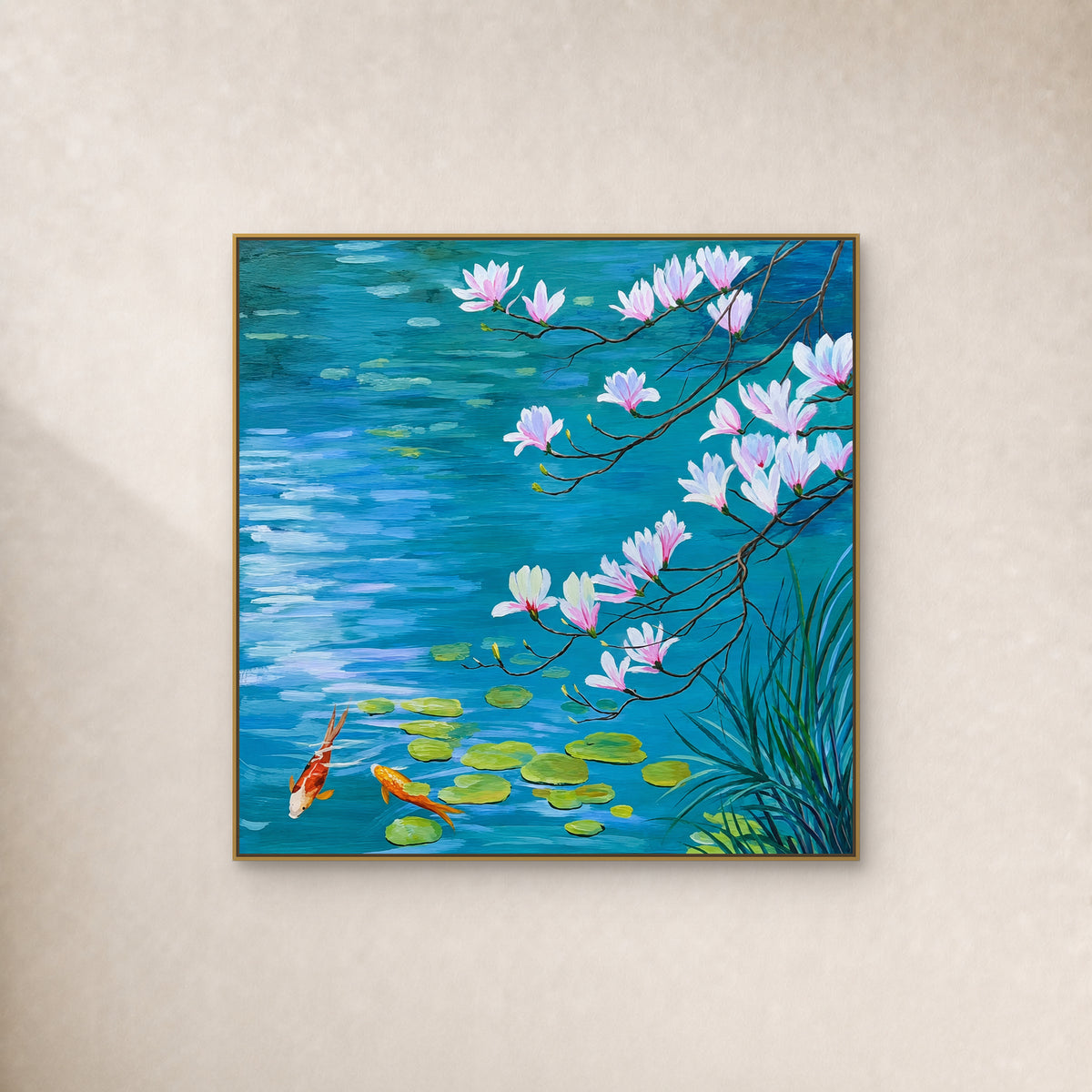 Square painting of pink magnolia branches over blue water with two koi, in a slim gold-tone frame on an ivory wall