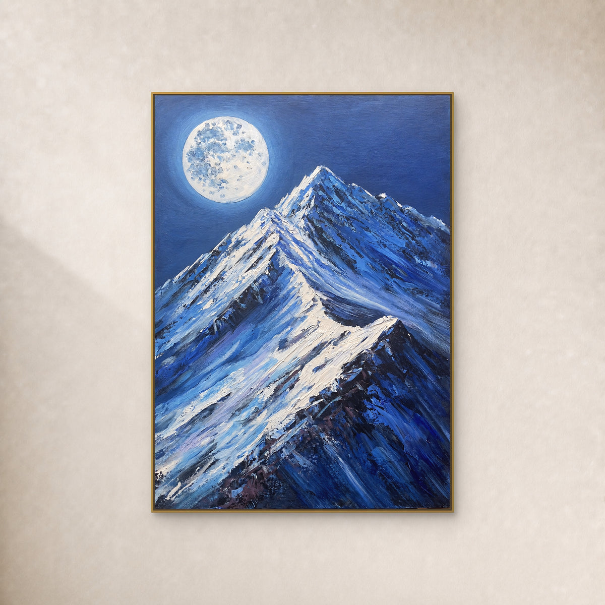 Pale full moon above blue snow peaks in a thin gold-tone floating frame on an ivory wall