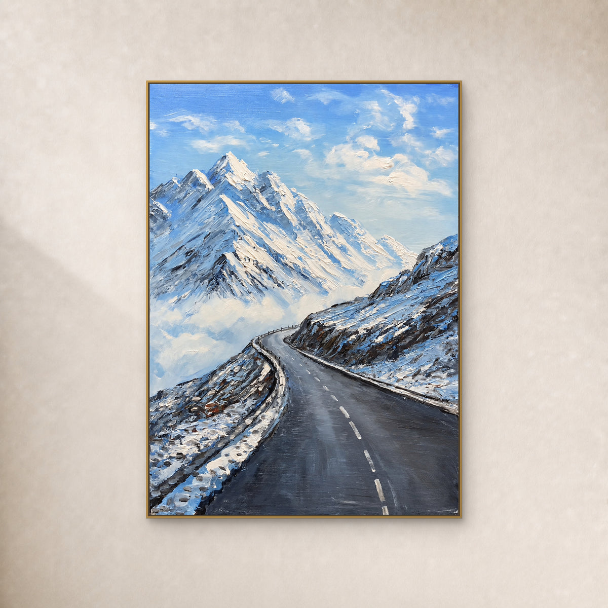 Snow peaks and a winding charcoal road in a thin gold floating frame against an ivory wall