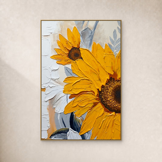Two yellow sunflowers with raised petals and blue-grey leaves in a slim gold-tone frame on an ivory wall