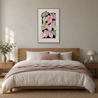 Vertical caladium leaf artwork in a wood-tone floating frame centred over an oak bed with ivory and dusty-rose bedding