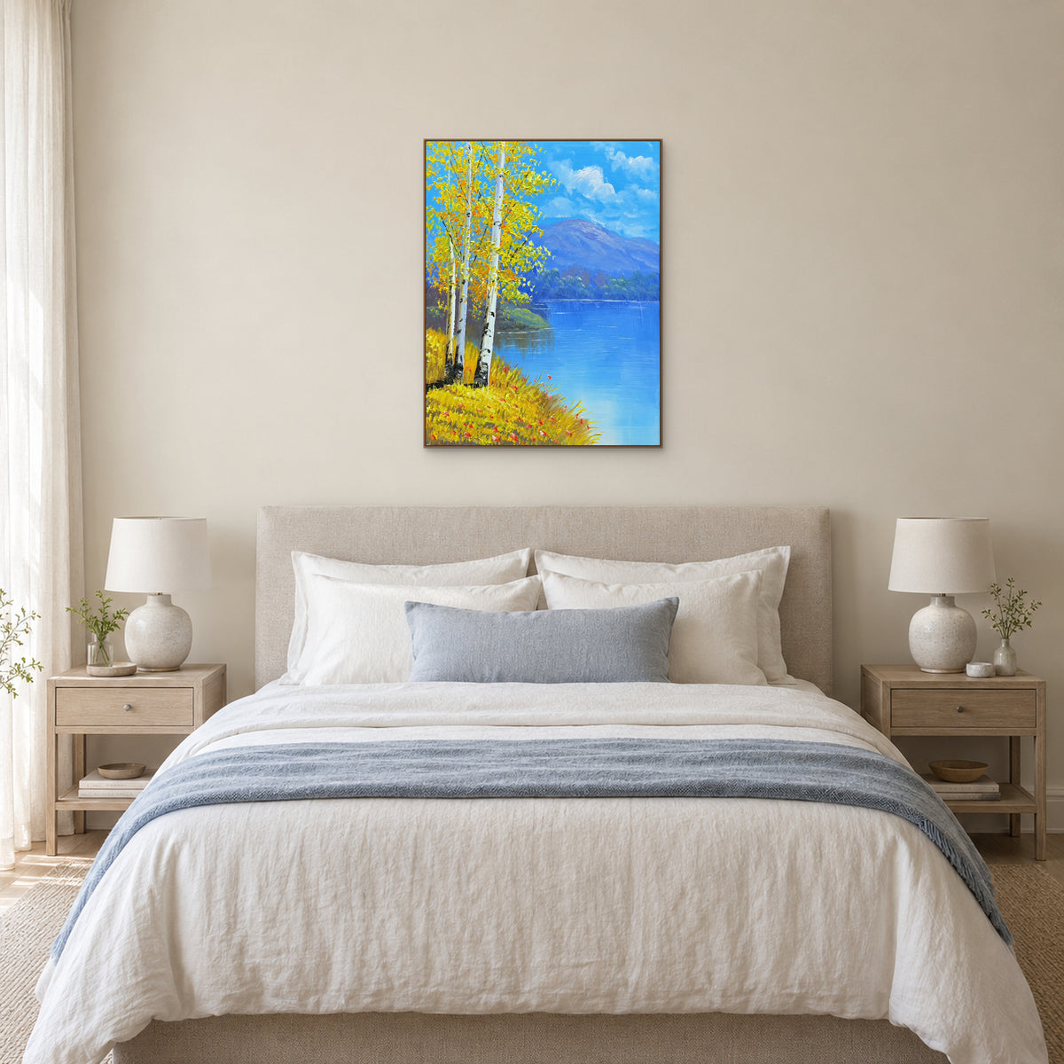 Yellow birch and blue lake painting in an oak-toned frame, centred above a cream upholstered bed.