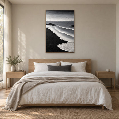 Black and white surf painting in a wood-tone floating frame centred above an oak-tone bed with ivory linen and a charcoal cushion