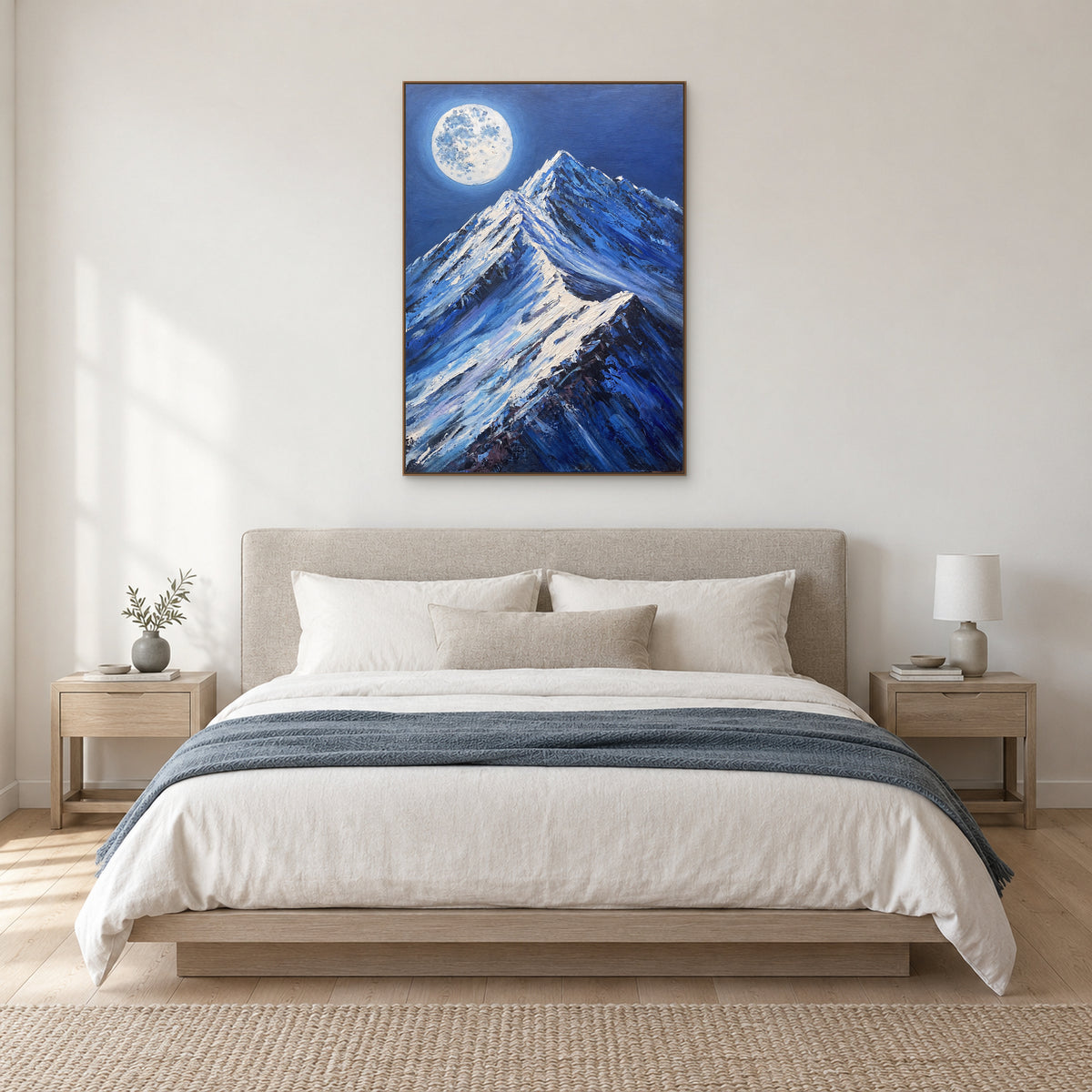 Moonlit blue mountain painting in a light wood-tone frame above a neutral upholstered bed