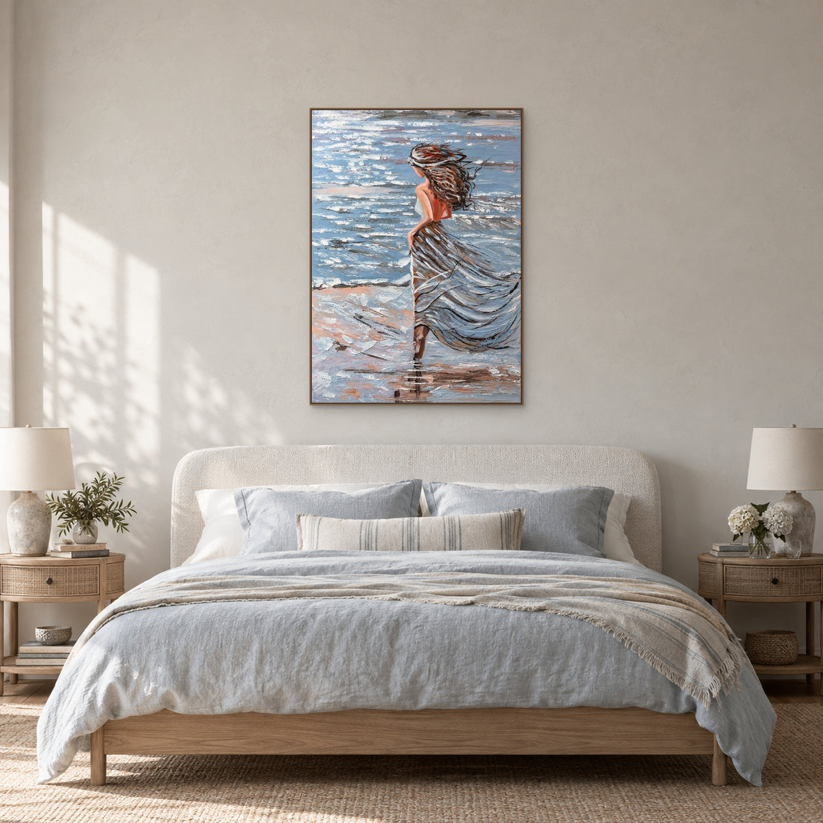 Coastal woman painting in an oak-toned floating frame centred above a rounded ivory headboard with pale blue bedding