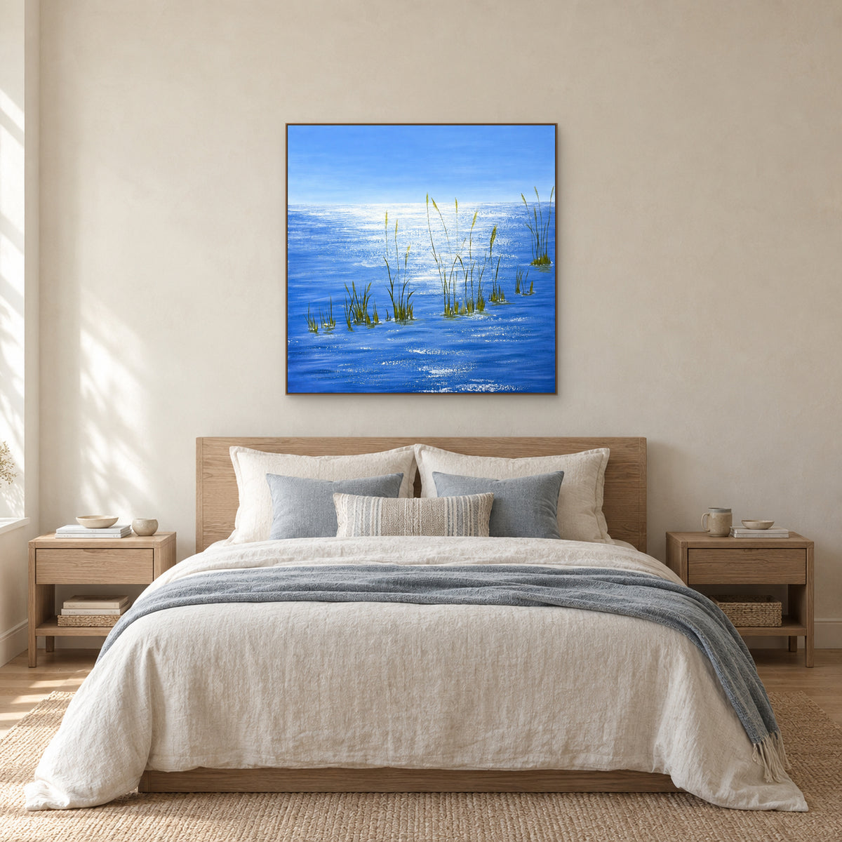 Blue water painting in an oak-tone floating frame centred above a pale linen bed