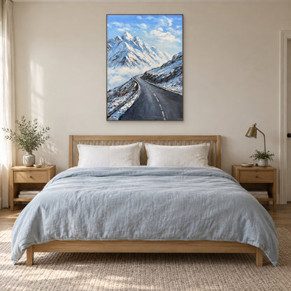 Vertical snow mountain painting in an oak-tone floating frame centred above a bed with pale blue bedding