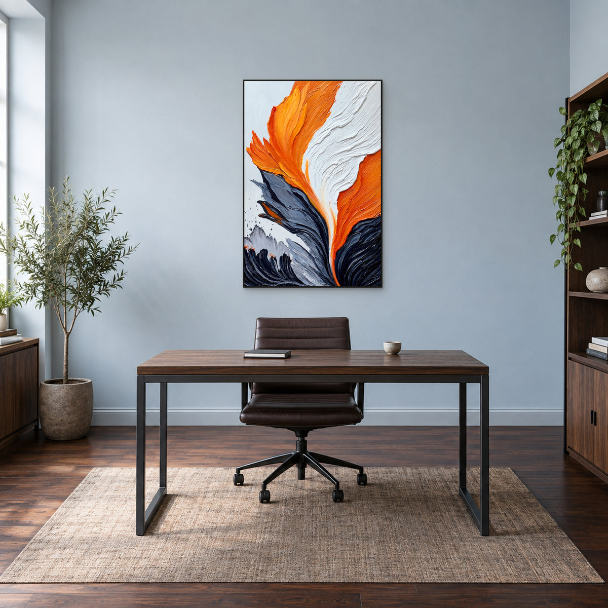 Orange and charcoal abstract painting in a thin black frame above a wooden desk against a blue-grey wall