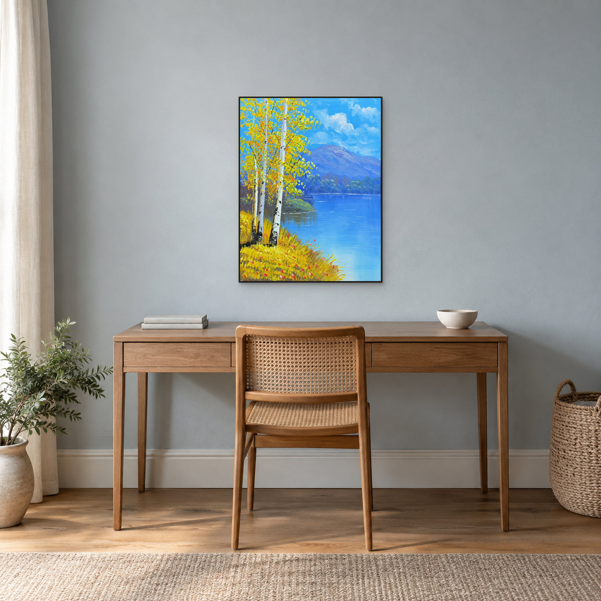 Autumn birches and an open blue lake in a thin black frame above a wooden writing desk.