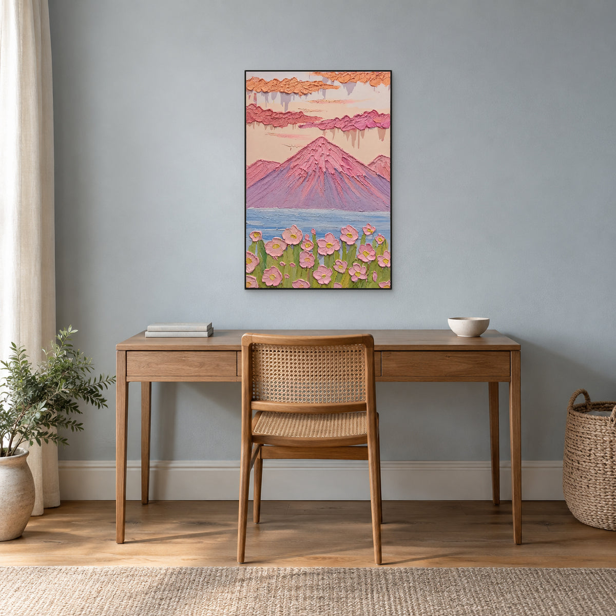 Pink mountain landscape in a slim black frame above a wooden desk against a blue-grey wall