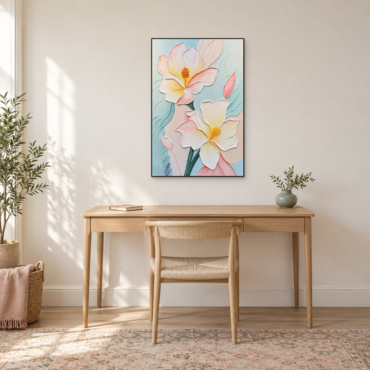 Vertical pastel flower painting in a thin black frame above a pale wooden desk and woven chair