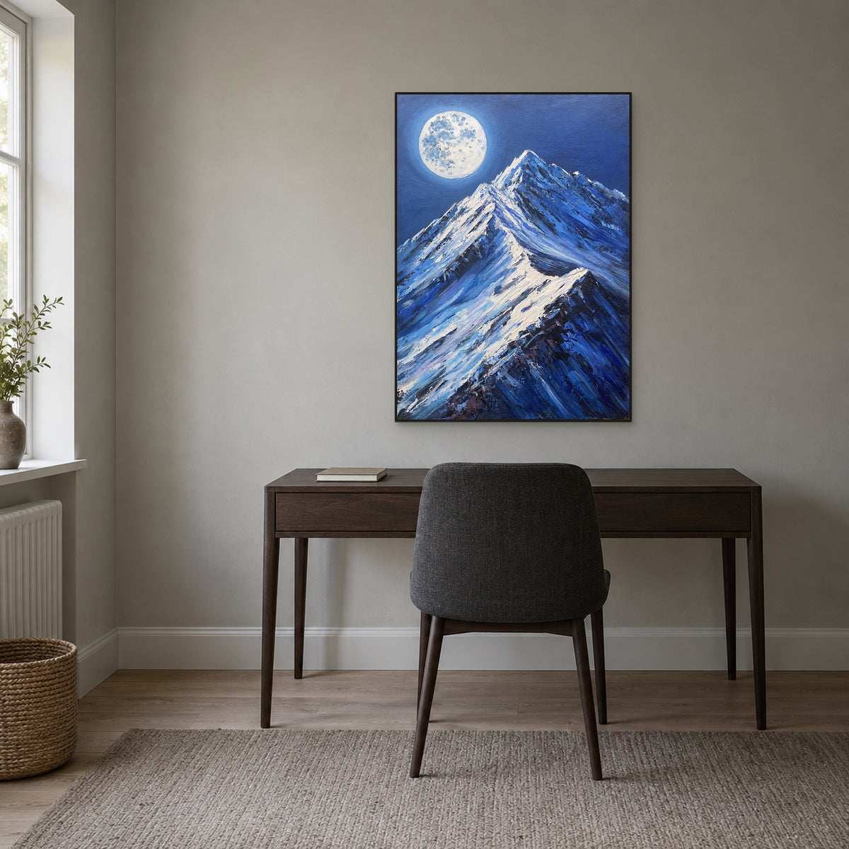 Snow peaks and full moon in a thin black frame aligned above a dark wooden desk