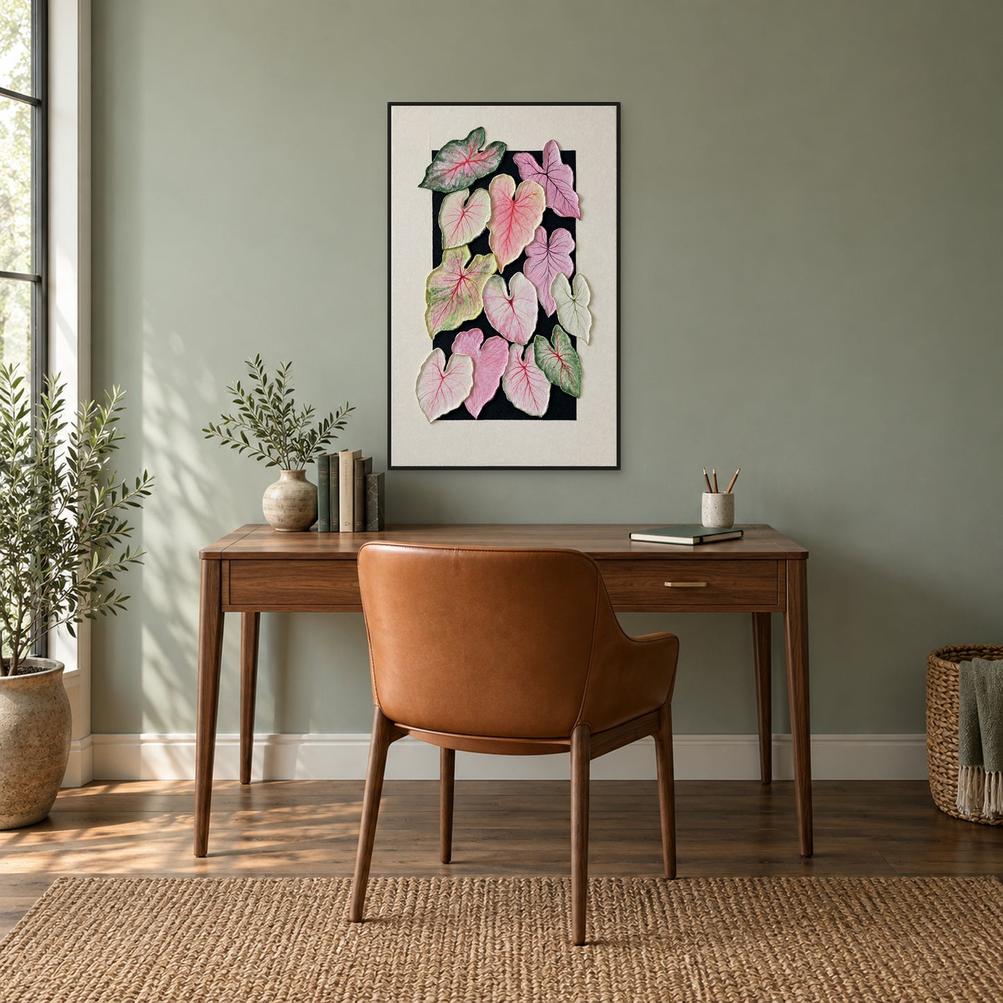 Pink and green caladium artwork in a black floating frame above a walnut desk on a muted green wall