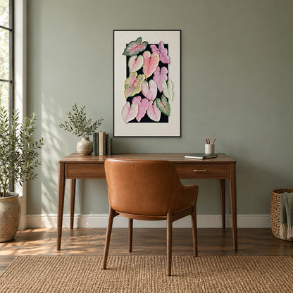 Pink and green caladium artwork in a black floating frame above a walnut desk on a muted green wall