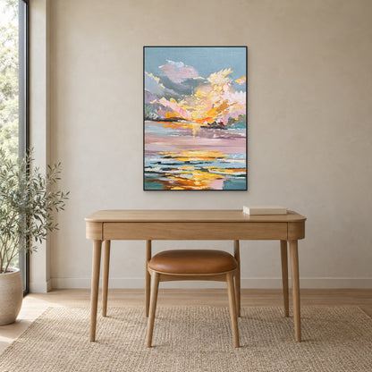 Pastel sunset and water reflections in a slim black frame above a light oak desk