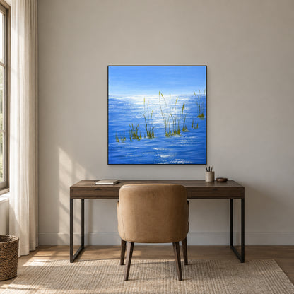 Square blue seascape in a thin black frame above a dark wood desk and tan chair