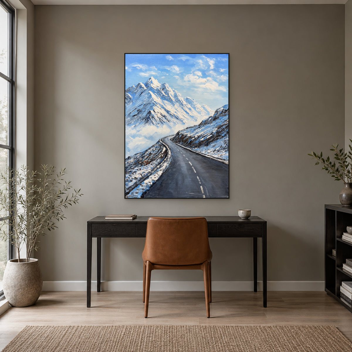 Mountain road painting in a black floating frame above a dark wooden desk and cognac-coloured chair