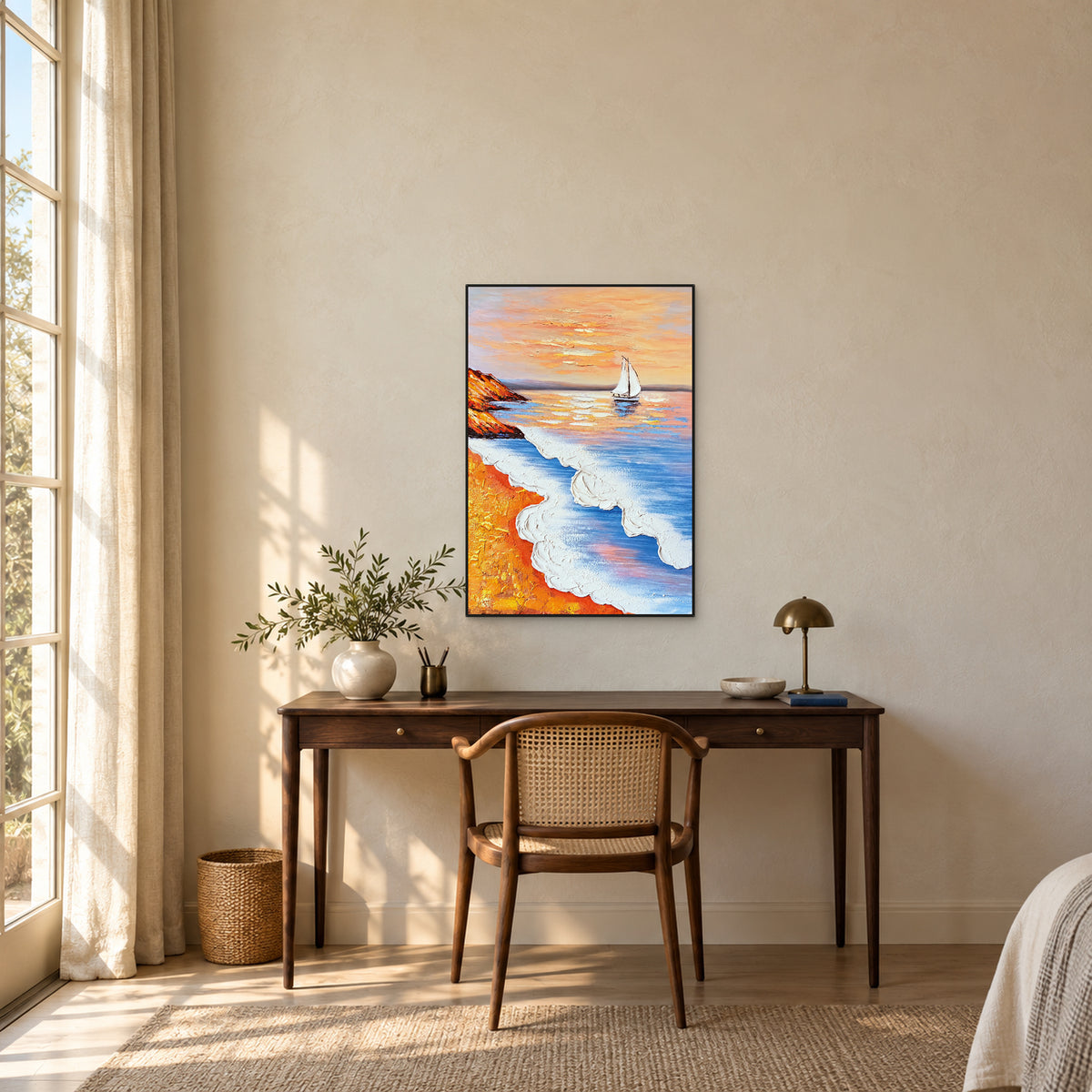 Vertical coastal painting in a black frame above a wooden desk, between a leafy vase and a brass-coloured lamp.