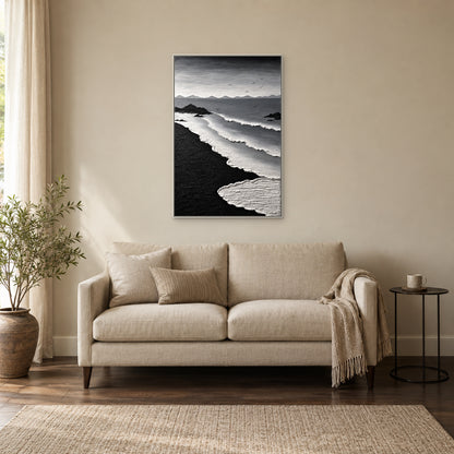 Textured white surf and black sand in a white floating frame above an oatmeal settee beside a window and a small black table