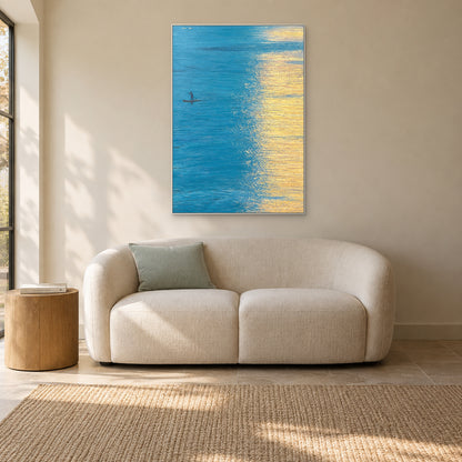 Golden Water in a thin white frame above a cream reading sofa