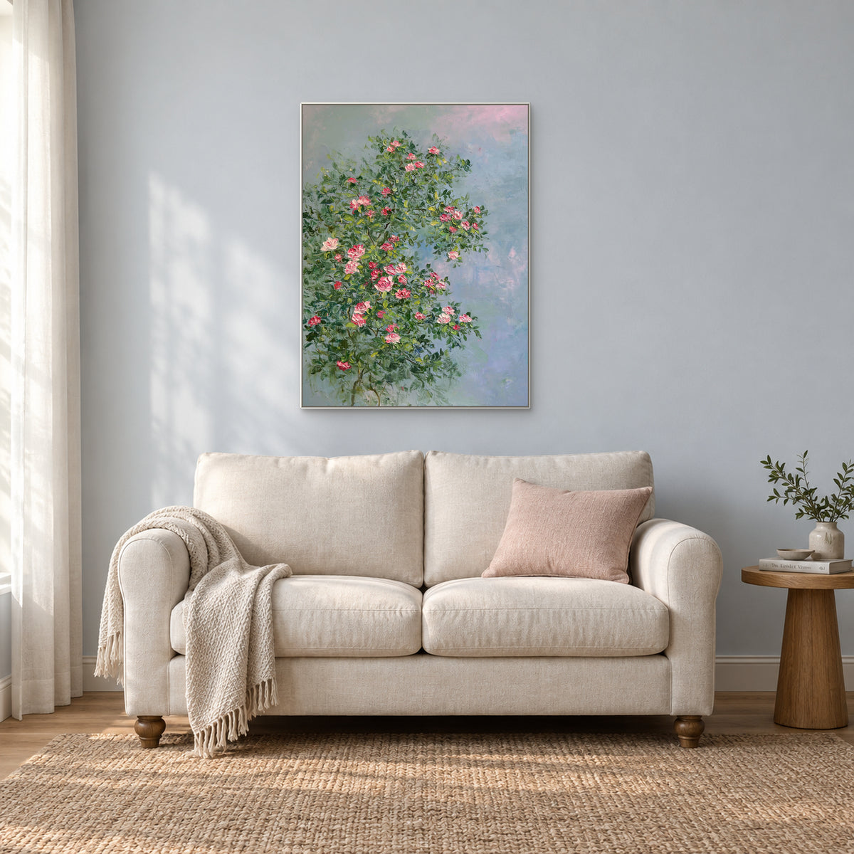 Pink rose painting in a thin white floating frame above a light upholstered loveseat in a reading nook