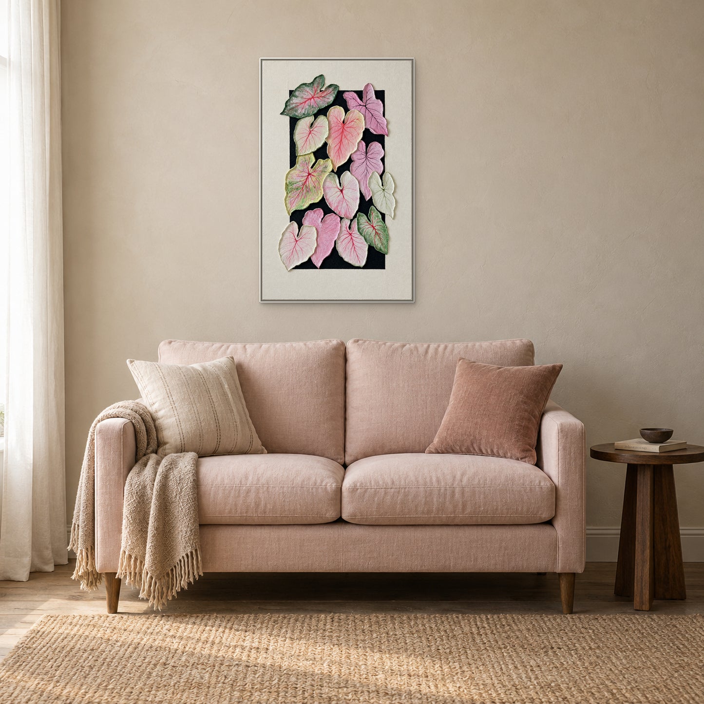 Caladium leaves in a white floating frame centred above a blush loveseat beside a small dark wood table