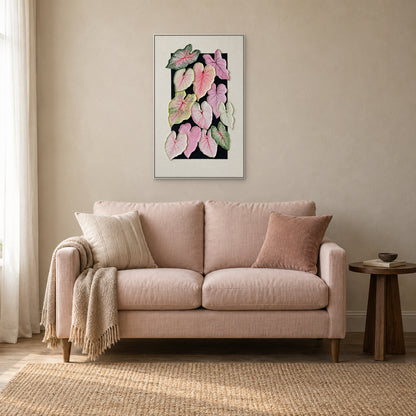 Caladium leaves in a white floating frame centred above a blush loveseat beside a small dark wood table