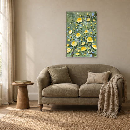 Yellow rose branches in a white floating frame above a curved beige loveseat beside a window