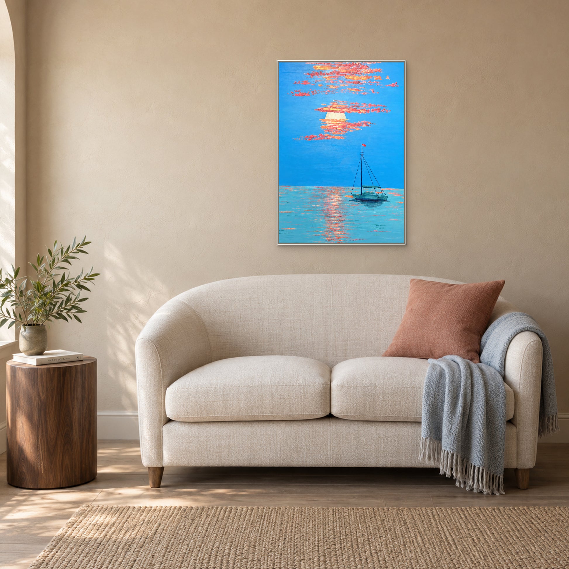 Vertical sunset seascape in a white floating frame above a cream loveseat with a coral cushion and pale blue throw.