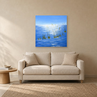 Shimmering blue water and grasses in a white floating frame above a cream loveseat