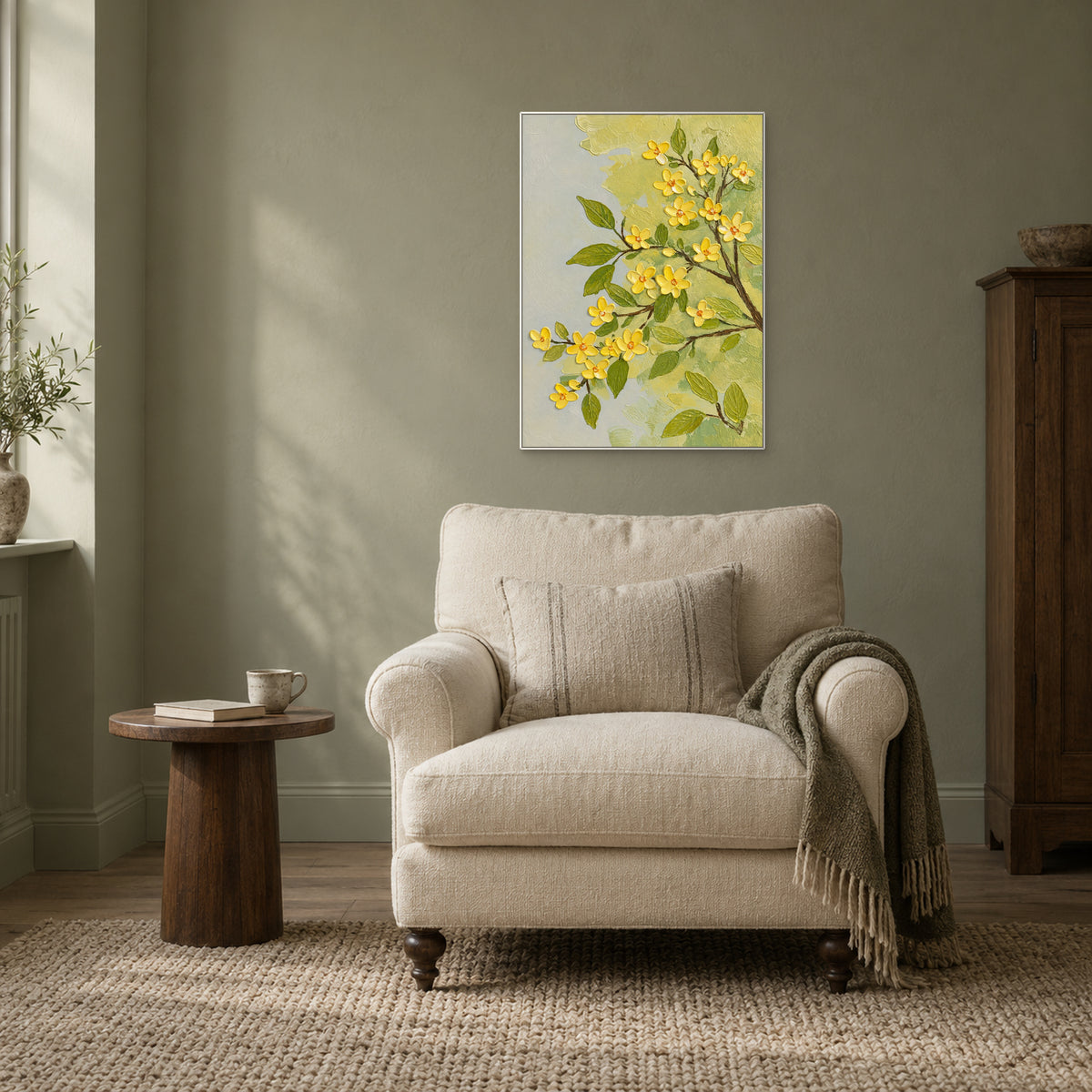 White-framed yellow blossom painting on a muted green wall above a cream reading chair