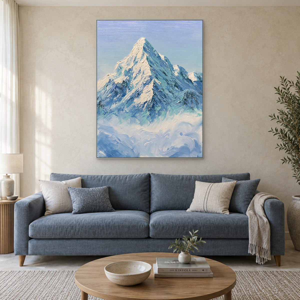 Blue mountain and white cloud painting in a silver-coloured frame, centred above a blue sofa.