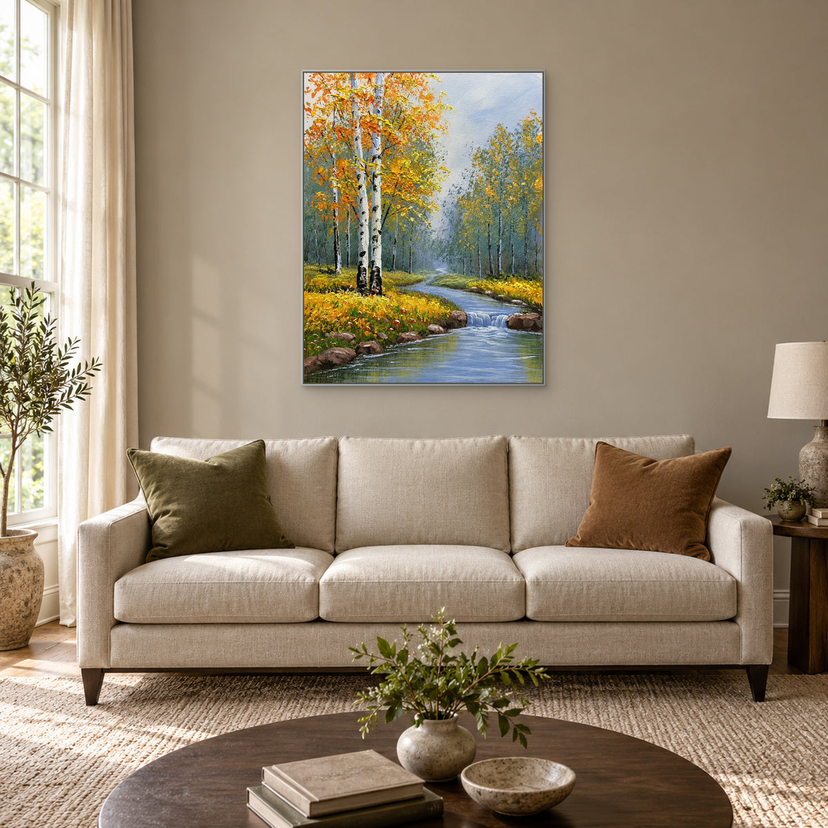 Vertical autumn birch landscape in a silver-tone frame above an off-white sofa with olive and brown cushions.