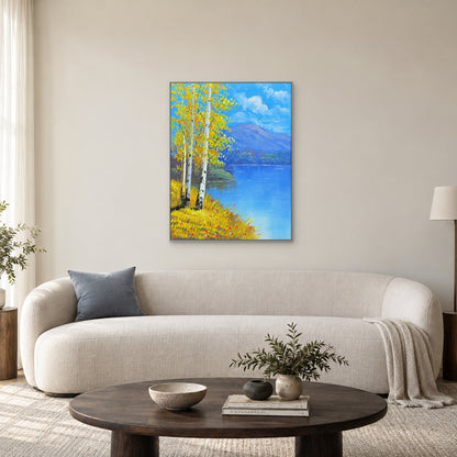 Bright yellow birches and blue water in a silver-toned frame above a curved ivory sofa.