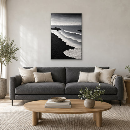 Monochrome coastal painting in a silver-tone floating frame centred above a charcoal sofa with ivory cushions and an oval wood coffee table