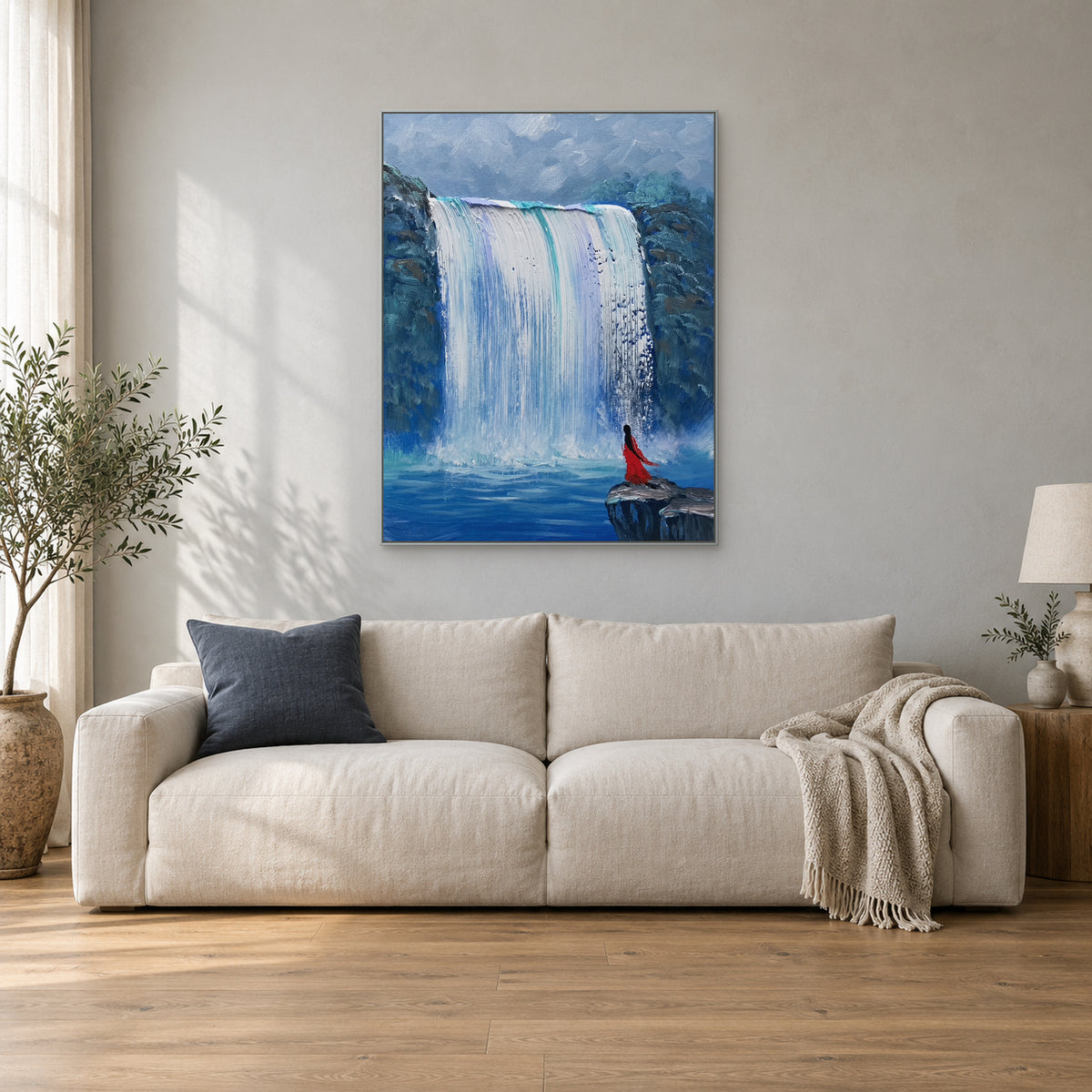 Blue waterfall with a red figure in a slim silver frame above a cream sofa with a slate-blue cushion.