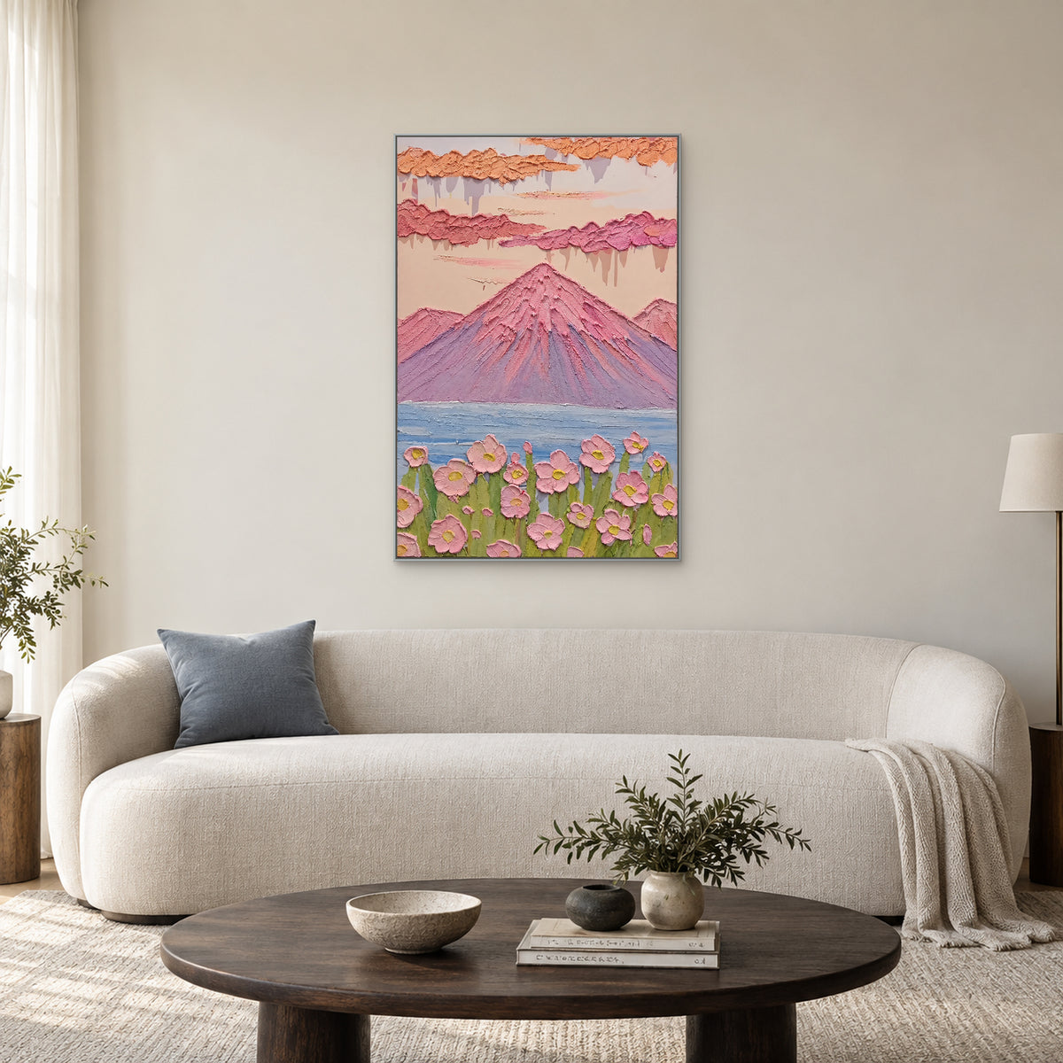 Vertical pastel mountain painting in a silver-tone frame above a curved ivory sofa