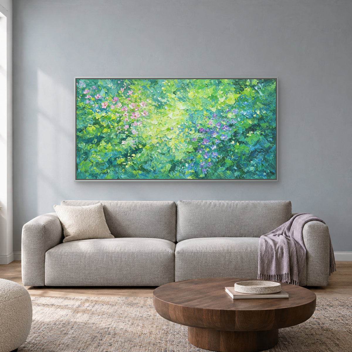 Horizontal green floral painting in a silver-toned floating frame above a pale grey sofa against a blue-grey wall