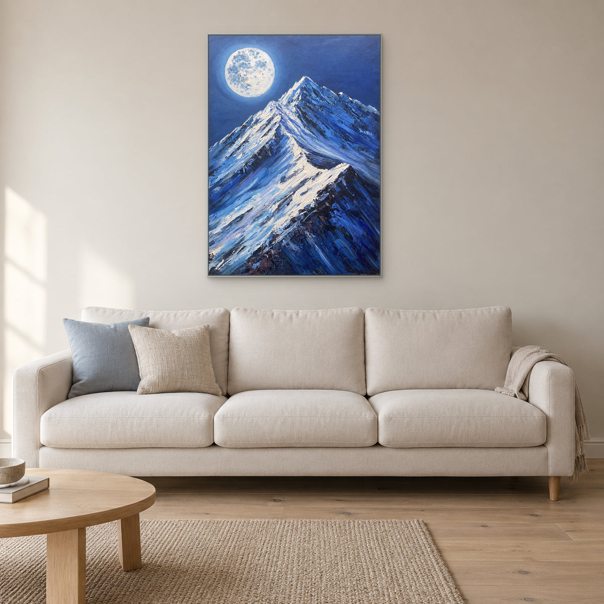 Silver-tone framed full moon and mountain painting above a cream sofa with blue and neutral cushions