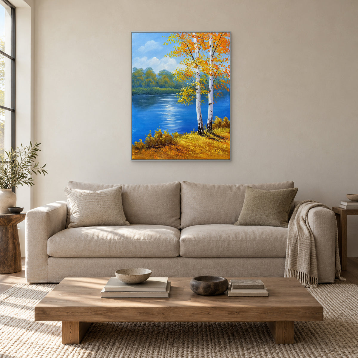 Two white birches and a blue river in a silver-coloured frame above a light living-room sofa